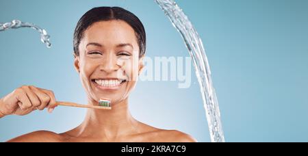 Schwarze Frau, Zahnbürste und Zähneputzen mit Wasserspritzer und Zahnpasta auf blauem Studiohintergrund für Zahngesundheit und Wellness. Hochformat und Stockfoto