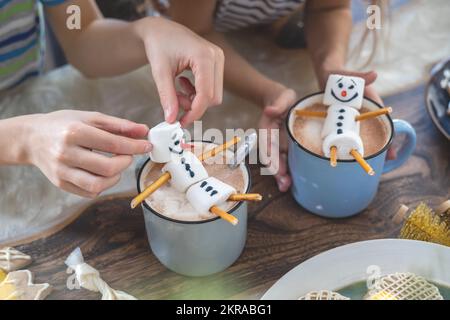 Kleine, süße Kinder essen einen Marmmelschnitzer, der mit Sahneschmuck und Getränken Kakao dekoriert ist. Stockfoto