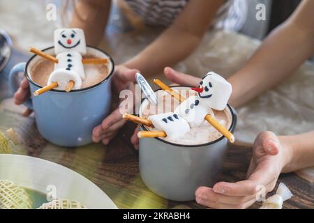 Kleine, süße Kinder essen einen Marmmelschnitzer, der mit Sahneschmuck und Getränken Kakao dekoriert ist. Stockfoto