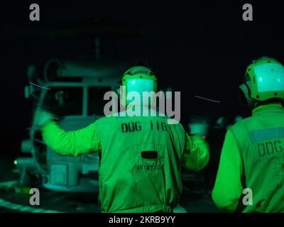 Boatswain’s Mate Seaman James Reyes-Ramirez signalisiert den Piloten eines MH-60R Sea Hawk, der an die „Spartaner“ des Helicopter Maritime Strike Squadron (HSM) 70 im Flugdeck des Arleigh Burke-Class Guided-Missile Destroyers USS Thomas Hudner (DDG 116) als Teil der Gerald Strike Group R. Ford angeschlossen ist. Am 11. November 2022 während der Übung Stille Wolverine. Übung Silent Wolverine ist eine von den USA geführte, kombinierte Trainingsübung, die die Fähigkeiten von Flugzeugträgern der Ford-Klasse durch integrierte High-End-Szenarien der Marine-Kriegsführung zusammen mit den teilnehmenden Verbündeten im Osteratlantik testet. T Stockfoto