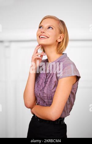 Ich Frage mich, was die Zukunft bringt. Eine schöne lächelnde junge Frau, die fürs Büro gekleidet ist. Stockfoto