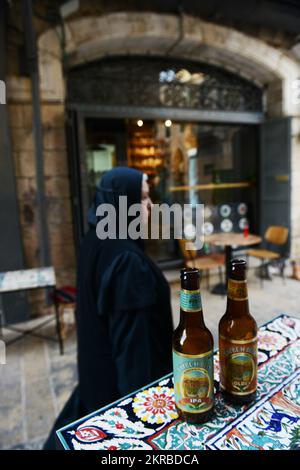 Genießen Sie ein kaltes palästinensisches Taybritbier in einem Café/einer Bar in der lebhaften New Gate Street im christlichen Viertel in der Altstadt von Jerusalem. Stockfoto