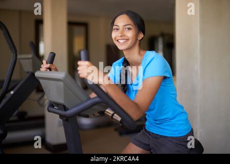 Ganzkörpertraining. Eine junge ethnische Frau, die im Fitnessstudio auf einem Heimtrainer trainiert. Stockfoto