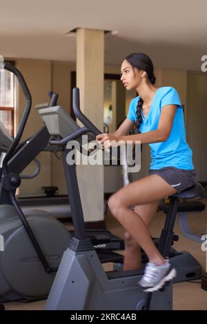 Ganzkörpertraining. Eine junge ethnische Frau, die im Fitnessstudio auf einem Heimtrainer trainiert. Stockfoto
