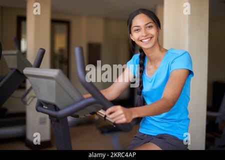 Ganzkörpertraining. Eine junge ethnische Frau, die im Fitnessstudio auf einem Heimtrainer trainiert. Stockfoto