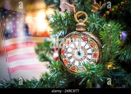 Weihnachtsbaumschmuck mit Uhren, die fünf Minuten bis Neujahr zeigen, mit us-Flagge im Hintergrund Stockfoto