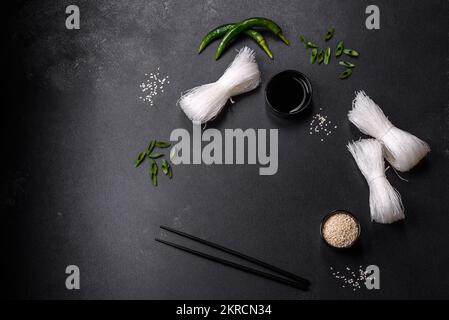 Leckeres Gericht der asiatischen Küche mit Reisnudeln, Huhn, Spargel, Pfeffer, Sesamsamen und Sojasauce auf dunklem Betonhintergrund Stockfoto