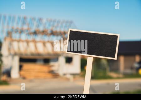 Die schwarze Plakatwand gegen das Haus wird gerade renoviert. Leere Mockup-Vorlage Blackboard Label Bau des Hauses. Platz kopieren nicht fertiggestelltes Gebäude. Renovierungsarbeiten. Privathaus mit Holzdach Entwicklung von Immobilien in modernen Stadtvororten Stockfoto