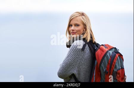 Genießen Sie eine einsame Wanderung. Porträt einer schönen jungen Frau, die mit einem Rucksack draußen steht. Stockfoto