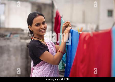 Eine Frau, die nasse Klamotten an der Wäscheleine im Garten aufhängt Stockfoto
