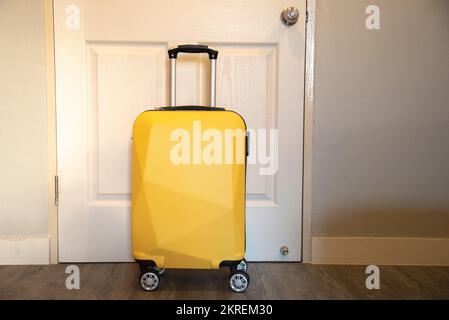 Gelber Reisekoffer im Schlafzimmer vor der Tür - entspannende Zeit, Urlaub, Wochenende und Reisekonzept. Stockfoto