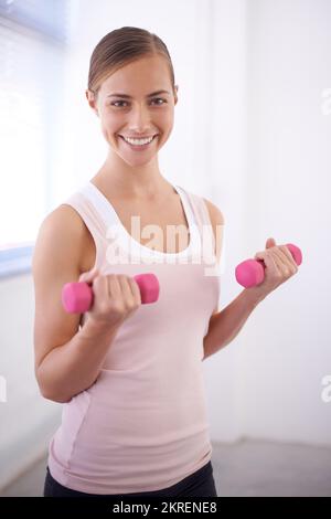 Sie ist motiviert, gesund und fit zu bleiben. Eine schöne junge Frau, die mit Gewichten trainiert. Stockfoto