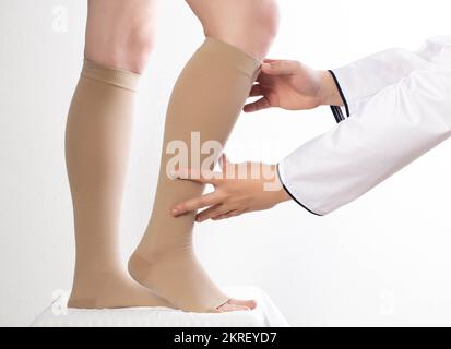 Der Arzt des Phlebologen wählt die Größe der Kompressionsstrümpfe des Patienten aus. Weißer Hintergrund, Nahaufnahme. Phlebitis Stockfoto