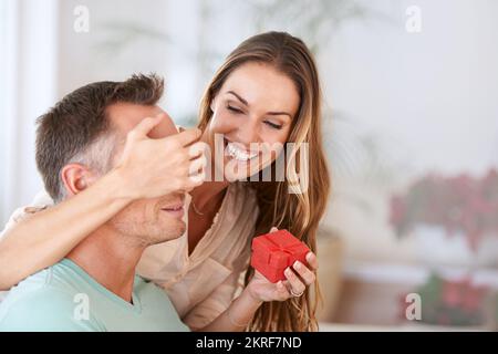 Ich habe etwas für dich. Eine Frau, die ihren Mann mit einem Geschenk überraschte. Stockfoto