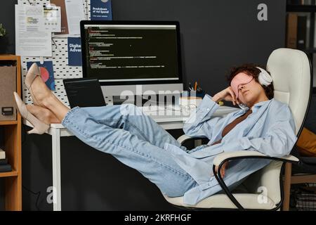Junge Geschäftsfrau mit Maske, die während des Arbeitstages im Büro am Arbeitsplatz schläft Stockfoto
