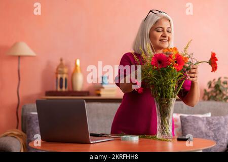 Eine alte Frau dekoriert zu Hause eine Vase mit Blumen Stockfoto