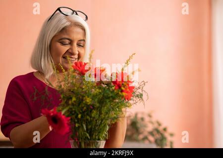 Eine alte Frau dekoriert zu Hause eine Vase mit Blumen Stockfoto