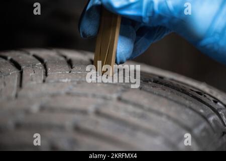 Renningen, Deutschland. 28.. November 2022. Ein Mitarbeiter in einer Werkstatt misst die Lauffläche der Reifen während der Wartung eines Elektroautos des Mazda MX-30. Kredit: Marijan Murat/dpa/Alamy Live News Stockfoto