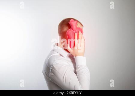 Ein Mann hält ein Heizkissen mit heißem Wasser in der Nähe seiner Wange. Zahnschmerzen, Infektion. Wärmebehandlung. Stockfoto
