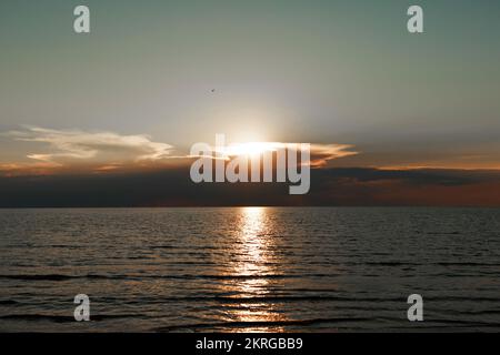 Wellen auf dem Meer bei Sonnenuntergang. Entspannung, Vergnügen. Reise zum Meer, Frieden und Glück. Farbenfroher, heller, orangefarbener Sonnenuntergang. Die Sonne scheint durch die Wolken auf dem Ozean. Schöne Tapeten für dein Handy. Hochwertige 4K-Aufnahmen. Stockfoto