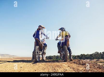 Zeit, die Bahn zu zerfetzen. Zwei Motocross-Fahrer, die sich vor einem Rennen unterhalten. Stockfoto