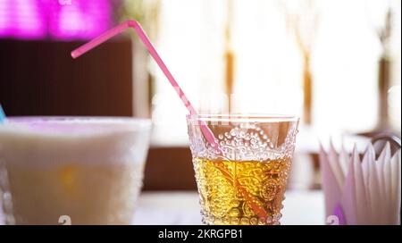 Apfelsaft in einem Glas auf einem Tisch mit einem Strohhalm vor dem Hintergrund eines Fensters und der Sonne. Sommergetränk. Stockfoto