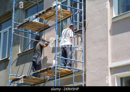 Bauunternehmer streichen Außenwände außerhalb der Hausfassade. Nahaufnahme des Malhauses an der Außenwand. Stockfoto