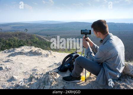Fotograf fotografiert in den Bergen mit Mobiltelefon und Stativ Stockfoto