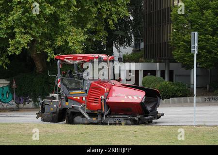 Roter Straßenfertiger mit Raupenketten ohne Fahrer steht auf der Straße. Stockfoto