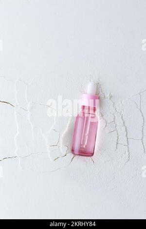 Feuchtigkeitsspendendes Serum in einer Flasche mit einer Pipette auf abstraktem Hintergrund mit Rissen, Hyaluronserum oder Toner oder Lotion, Gesichts- und Körperpflege Stockfoto