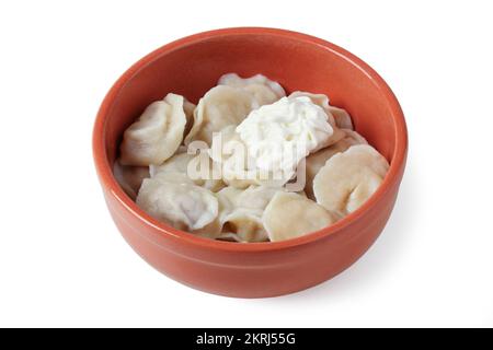 Gekochte Teigtaschen mit saurer Sahne in einem Tonbecher, isoliert auf Weiß Stockfoto