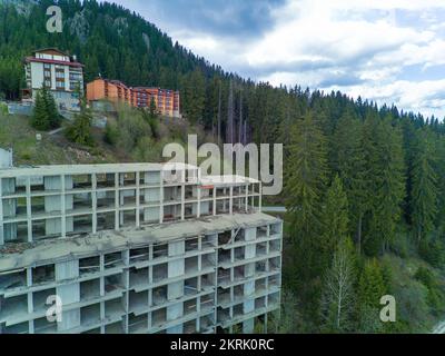 Das mehrstöckige verlassene Hotel mit Betonwänden befindet sich in einem dichten Fichtenwald am Hang des hohen Tals der Rhodope Mountains Stockfoto