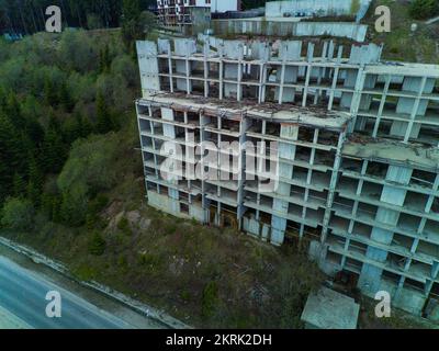 Das mehrstöckige verlassene Hotel mit Betonwänden befindet sich in einem dichten Fichtenwald am Hang des hohen Tals der Rhodope Mountains Stockfoto