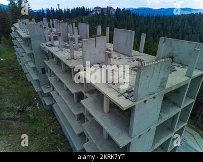 Das mehrstöckige verlassene Hotel mit Betonwänden befindet sich in einem dichten Fichtenwald am Hang des hohen Tals der Rhodope Mountains Stockfoto