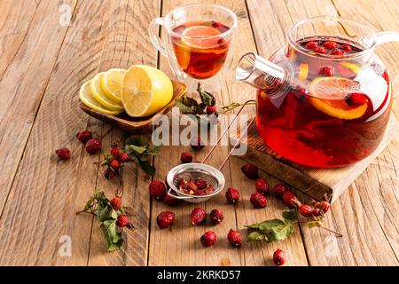 Heißer Vitamintee mit Rosenhüften steht auf einem hölzernen Podium und einem Tisch mit einer Tasse Tee und Zitronenscheiben. Phytotherapie. Kalte Getränke Stockfoto