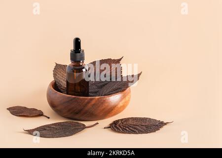 Anti-Aging-Serum oder Kosmetikum in einer Glasflasche mit Pipette in einer Holzschüssel mit braunen Blättern auf beigem Hintergrund. Vorderansicht Stockfoto