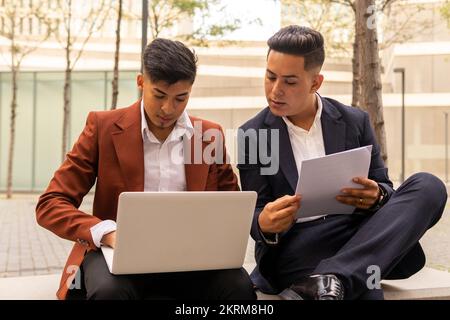 Fokussierte hispanische Geschäftsleute in eleganten Outfits mit Dokumentation über Laptop, während sie gemeinsam an einem Projekt arbeiten Stockfoto