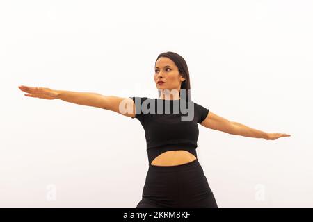 Konzentrierte Sportlerin in enger schwarzer Sportkleidung, die Yoga praktiziert und Virabhadrasana B trainiert, Balancierung und Meditation gegen weißen Hintern Stockfoto