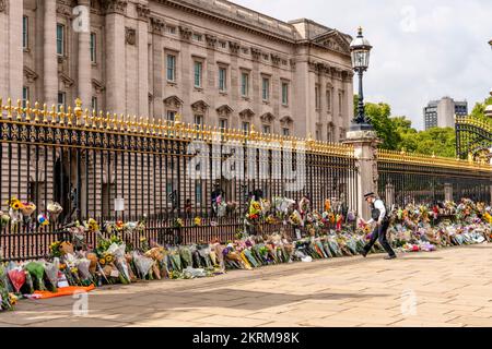 Ein Polizist platziert Blumen, die Ihm Von Einem Mitglied der Öffentlichkeit gegeben wurden, vor den Toren des Buckingham Palace nach dem Tod der Königin, London, Großbritannien. Stockfoto