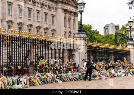 Ein Polizist platziert Blumen, die Ihm Von Einem Mitglied der Öffentlichkeit gegeben wurden, vor den Toren des Buckingham Palace nach dem Tod der Königin, London, Großbritannien. Stockfoto