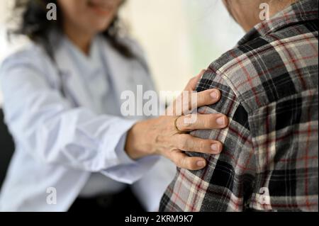 Professionelle und friedliche asiatische Chefarzt berührt die Schulter ihrer jungen Patientin, unterstützt sie und beruhigt sie während der medialen Untersuchung. cl Stockfoto