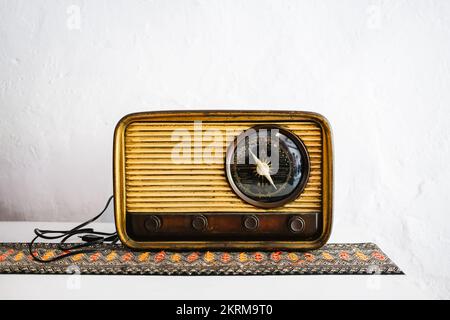 Retro-Radio in Vintage-Holzfarbe auf dem Tisch auf verziertem Stoff an der weißen Wand Stockfoto