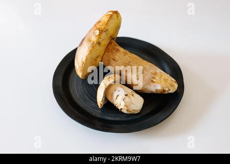 Von oben: Porcini-Pilze auf schwarzer, runder Keramikplatte auf weißem Hintergrund Stockfoto