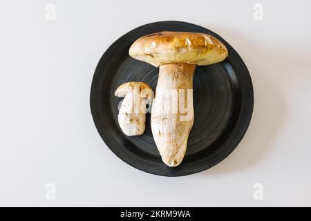 Von oben: Porcini-Pilze auf schwarzer, runder Keramikplatte auf weißem Hintergrund Stockfoto