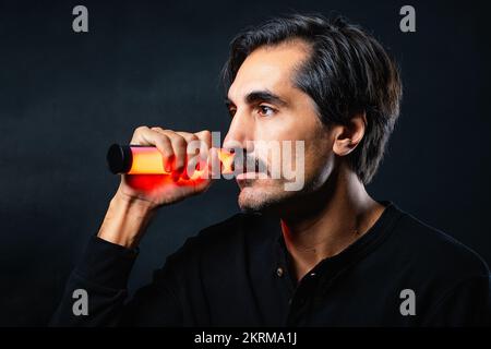 Seitenansicht eines Mannes mit Schnurrbart in schwarzer Kleidung, der wegblickt, während er im Studio steht, mit orangefarbener Neonröhrenlampe im Gesicht Stockfoto