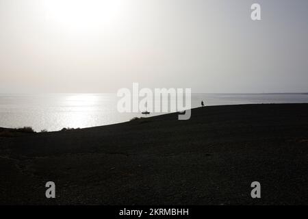 Silhouette eines unbekannten Touristen, der auf einem sandigen Hügel steht und die atemberaubende Landschaft des endlos rauschenden Ozeans bei Sonnenuntergang am Aussichtspunkt on Play bewundert Stockfoto