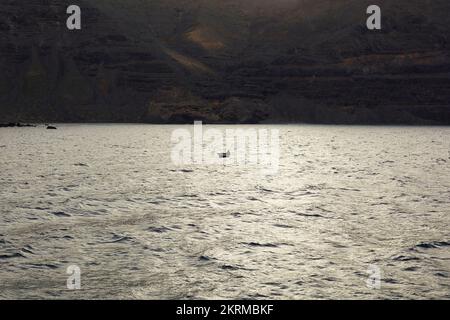 Kleines Motorboot, das im Wellenmeer in der Nähe des riesigen felsigen Vulkans bei Sonnenuntergang in La Graciosa auf den Kanarischen Inseln schwimmt Stockfoto