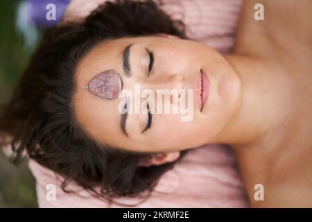 Blick von oben auf eine entspannende Frau mit geschlossenen Augen und Massagestein auf der Stirn während der Spa-Sitzung Stockfoto