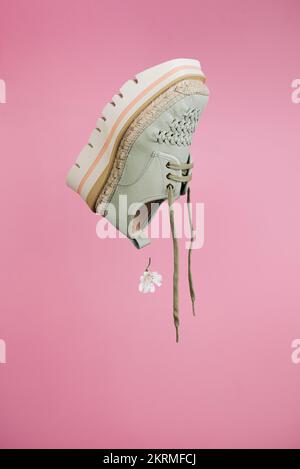Winzige weiße Blume, die im Sommer aus dem stilvollen Schuh fällt und vor pinkfarbenem Hintergrund schwebt Stockfoto