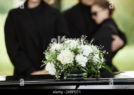 Nahaufnahme des Blumenstraußes auf dem Sarg mit Menschen im schwarzen Hintergrund, Beerdigungszeremonie im Freien, Kopierraum Stockfoto